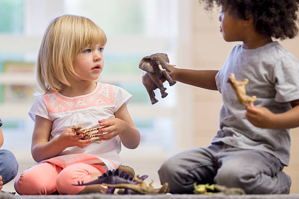 A multi-ethnic group of elementary age children are playing together with plastic animal toys at day care.